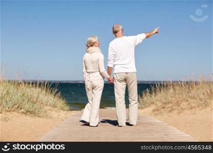 family, age, travel, tourism and people concept - happy senior couple holding hands and pointing finger on summer beach