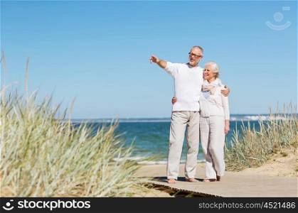 family, age, travel, tourism and people concept - happy senior couple hugging and pointing finger on summer beach