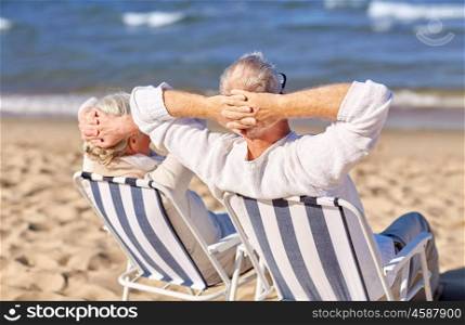 family, age, travel, tourism and people concept - happy senior couple sitting on deck chairs on summer beach