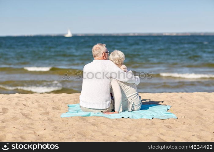 family, age, travel, tourism and people concept - happy senior couple sitting on plaid and hugging on summer beach