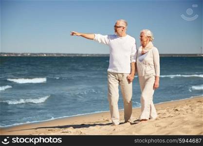 family, age, travel, tourism and people concept - happy senior couple walking and pointing finger to something on summer beach