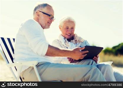 family, age, travel, tourism and people concept - happy senior couple with tablet pc computer sitting on deck chairs on summer beach