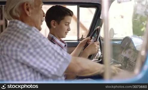 Family and generation gap. Old grandpa spending time with his grandson. The senior man talks about vintage car with the boy and lean against the hood of an automobile from the 50s