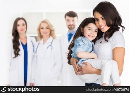 Family and group of doctors. Young mother with daughter and droup of doctors on background in hospital