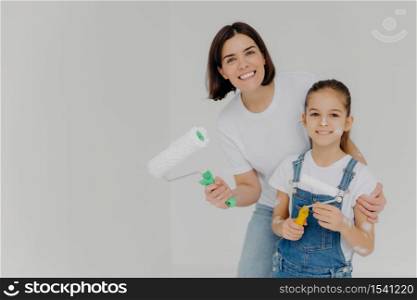 Family and house repairing concept. Positive caring mother cuddles child, have fun when refurbish walls, dressed in casual domestic clothes, hold repir tools, isolated over white background.