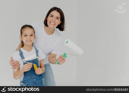 Family and house repairing concept. Positive caring mother cuddles child, have fun when refurbish walls, dressed in casual domestic clothes, hold repir tools, isolated over white background.