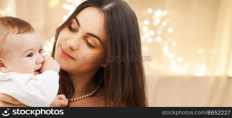 family and motherhood concept - close up of happy smiling young mother with little baby over christmas lights background. close up of mother with baby over christmas lights