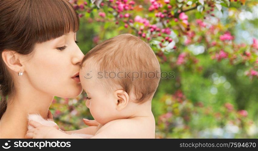 family and motherhood concept - close up of happy young mother kissing little baby over natural spring cherry blossom background. close up of happy mother kissing baby over garden