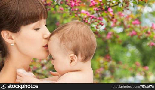 family and motherhood concept - close up of happy young mother kissing little baby over natural spring cherry blossom background. close up of happy mother kissing baby over garden