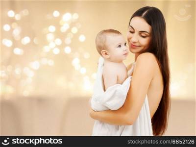 family and motherhood concept - close up of mother with baby in bath towel over christmas lights background. close up of mother with baby over christmas lights