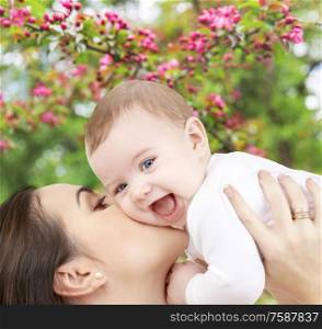 family and motherhood concept - close up of young mother kissing happy little baby over natural spring cherry blossom background. close up of mother kissing baby over garden