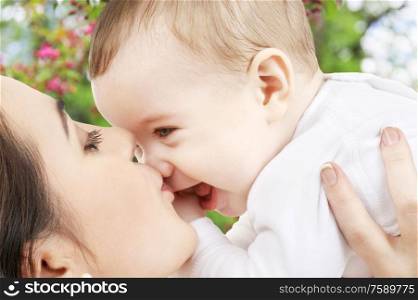 family and motherhood concept - close up of young mother kissing happy little baby over natural spring cherry blossom background. close up of mother kissing baby over garden