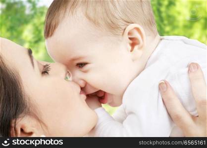 family and motherhood concept - happy smiling young mother kissing little baby over green natural background. mother kissing baby over green natural background