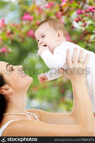 family and motherhood concept - happy smiling young mother with little baby over natural spring cherry blossom background. mother with baby over spring garden background