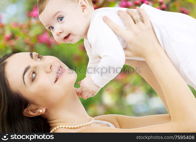 family and motherhood concept - happy smiling young mother with little baby over natural spring cherry blossom background. mother with baby over spring garden background