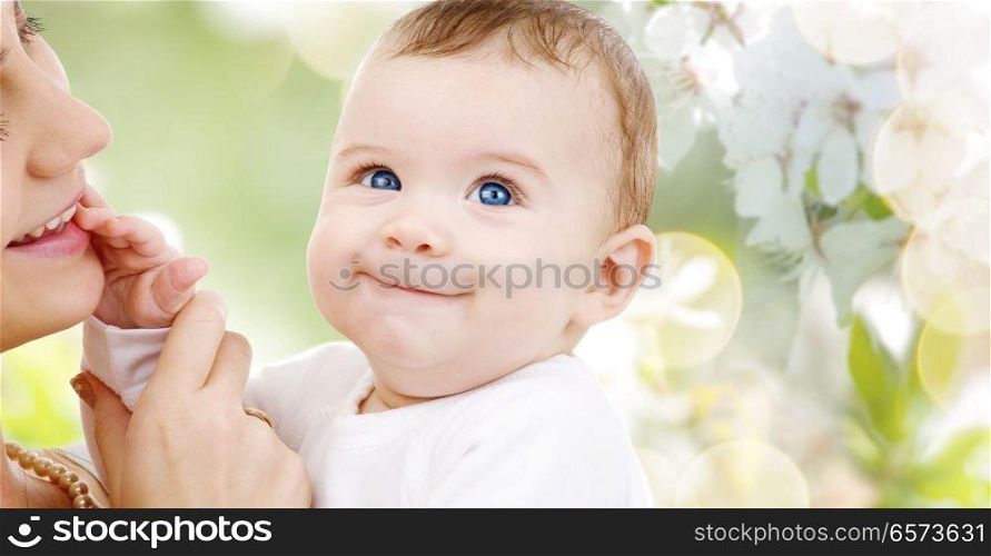 family and motherhood concept - happy smiling young mother with little baby over cherry blossom background. mother with baby over cherry blossom background