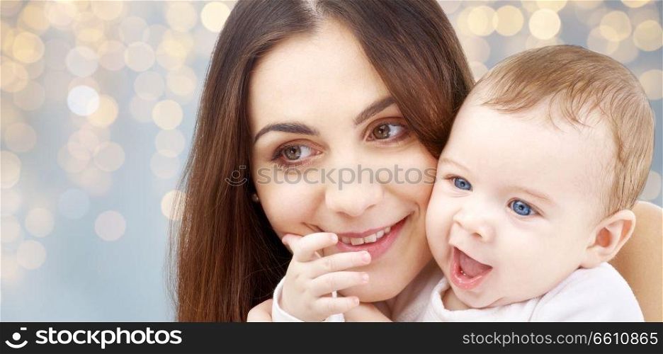 family and motherhood concept - happy smiling young mother with little baby over festive lights background. mother with baby over festive lights background