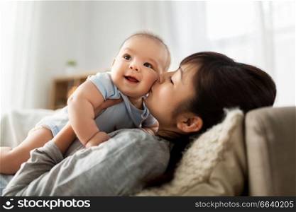 family and motherhood concept - happy young asian mother kissing little baby son at home. happy mother kissing little baby son at home