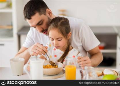 family and people concept - happy father and daughter eating flakes for breakfast at home. happy family eating flakes for breakfast at home