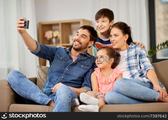 family and people concept - happy father, mother, little son and daughter taking selfie by smartphone at home. happy family taking selfie at home