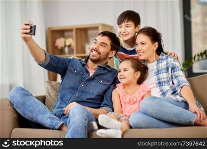 family and people concept - happy father, mother, little son and daughter taking selfie by smartphone at home. happy family taking selfie at home