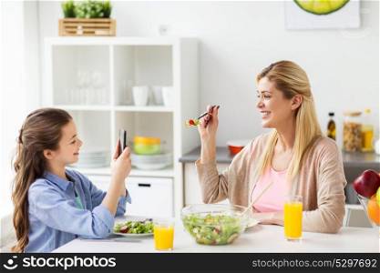 family and people concept - happy girl with smartphone having dinner and photographing her mother at home kitchen. girl photographing mother by smartphone at home