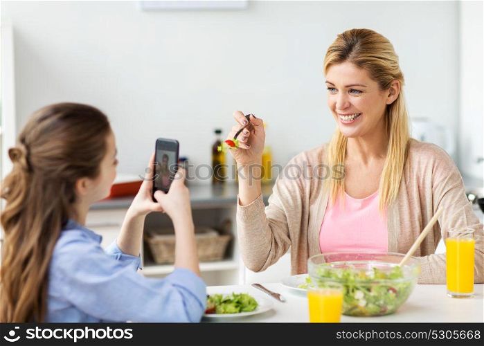 family and people concept - happy girl with smartphone having dinner and photographing her mother at home kitchen. girl photographing mother by smartphone at home