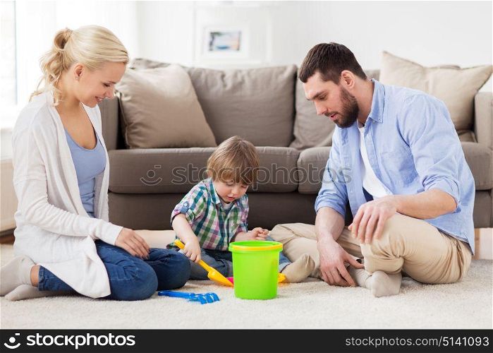 family and people concept - happy little boy and parents playing with beach sand toys set at home. happy family playing with beach toys at home
