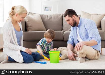family and people concept - happy little boy and parents playing with beach sand toys set at home. happy family playing with beach toys at home