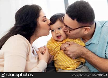 family and people concept - happy mother and father kissing baby son at home. happy mother and father kissing baby son at home