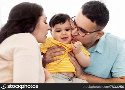 family and people concept - happy mother and father kissing baby son at home. happy mother and father kissing baby son at home