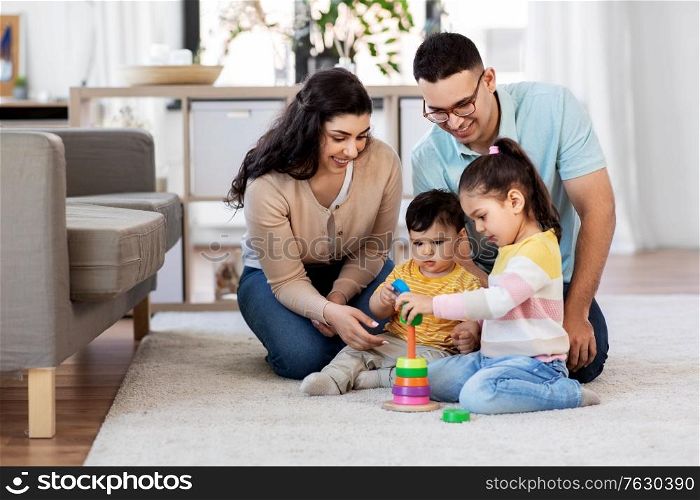 family and people concept - happy mother, father, little daughter and baby son playing with pyramid toy at home. happy family playing with pyramid toy at home