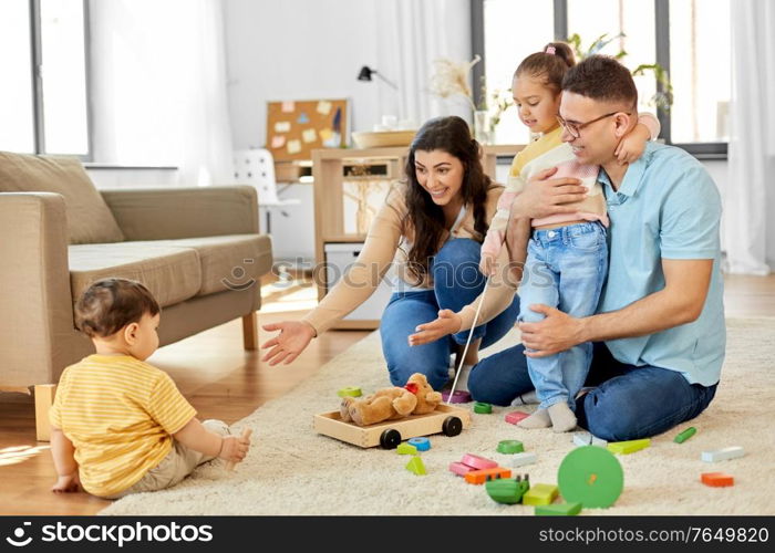 family and people concept - happy mother, father, little daughter and baby son playing with wooden toys at home. happy family palying with wooden toys at home