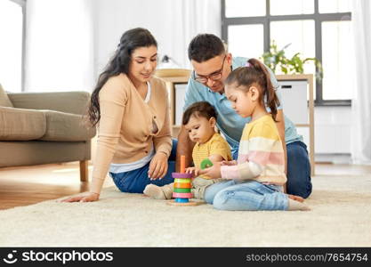 family and people concept - happy mother, father, little daughter and baby son playing with pyramid toy at home. happy family playing with pyramid toy at home