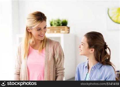 family and people concept - happy smiling mother and daughter at home kitchen. happy smiling family of woman and girl at home