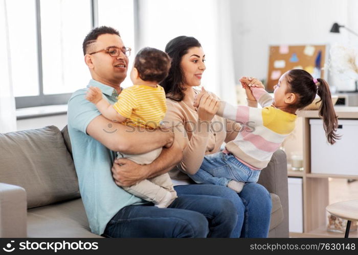 family and people concept - portrait of happy mother, father, little daughter and baby son sitting on sofa at home. portrait of happy family sitting on sofa at home