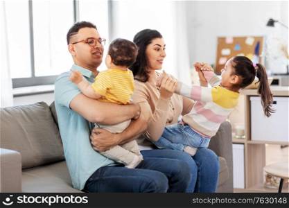 family and people concept - portrait of happy mother, father, little daughter and baby son sitting on sofa at home. portrait of happy family sitting on sofa at home