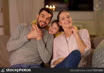 family and people concept - portrait of happy smiling father, mother and little daughter sitting on sofa at home at night. portrait of happy family sitting on sofa at home