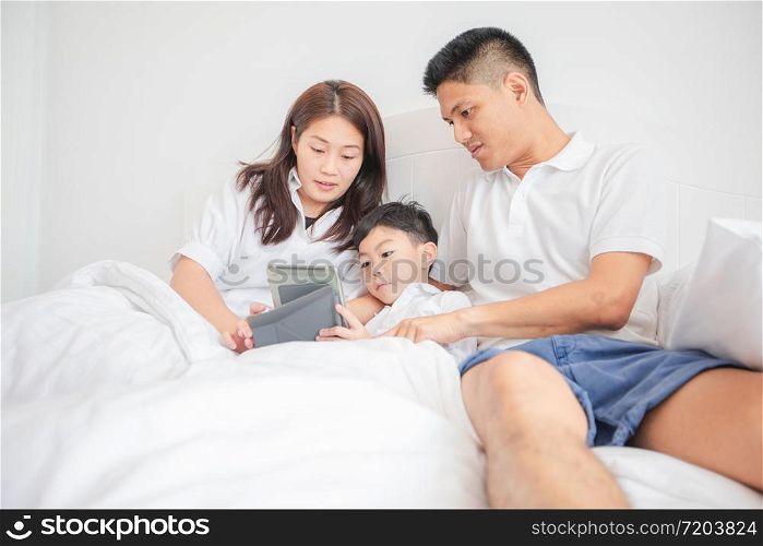 family and son watching and play tablet on bed