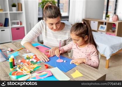 family, art and craft concept - mother spending time with her little daughter making applique of color paper at home. daughter with mother making applique at home