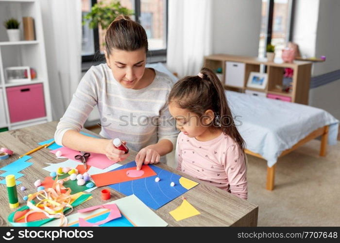 family, art and craft concept - mother spending time with her little daughter with glue making applique of color paper at home. daughter with mother making applique at home