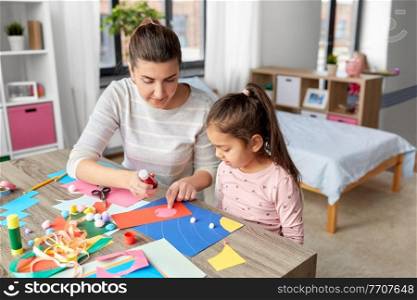 family, art and craft concept - mother spending time with her little daughter with glue making applique of color paper at home. daughter with mother making applique at home