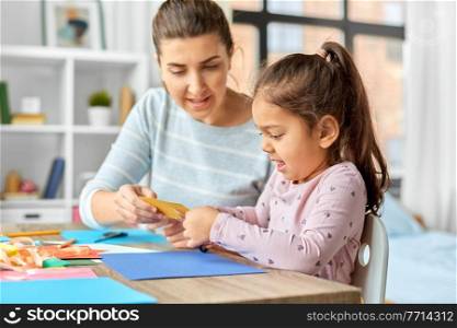 family, art and craft concept - mother spending time with her little daughter with glue making applique of color paper at home. daughter with mother making applique at home