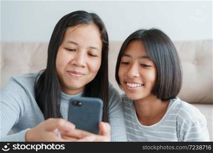 Family Asian mother and daughter using on smartphone together at home. Happy girl and mum while sitting in the living room togetherness. Close-up on face child and mom