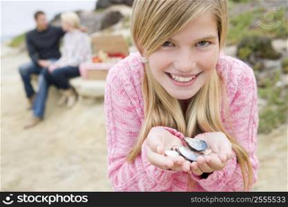 Family at beach with picnic smiling focus on girl with seashells