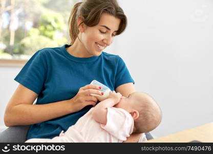 family, babyhood and people concept - mother feeding baby daughter with milk formula from bottle. mother feeding baby daughter with milk formula