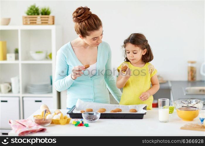 family, baking, cooking and people concept - happy mother and little daughter eating cookies at home kitchen. happy mother and daughter eating cookies at home
