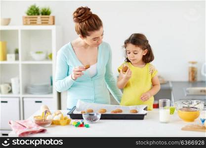 family, baking, cooking and people concept - happy mother and little daughter eating cookies at home kitchen. happy mother and daughter eating cookies at home