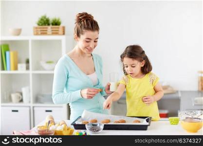 family, baking, cooking and people concept - happy mother and little daughter eating cookies with milk at home kitchen. happy mother and daughter eating cookies at home