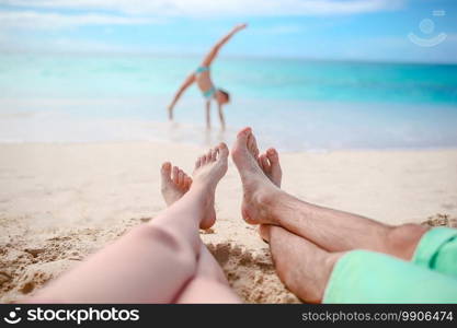 Family beach vacation. Closeup legs on the background of little kid making sporty exercises. Happy beautiful family on the beach